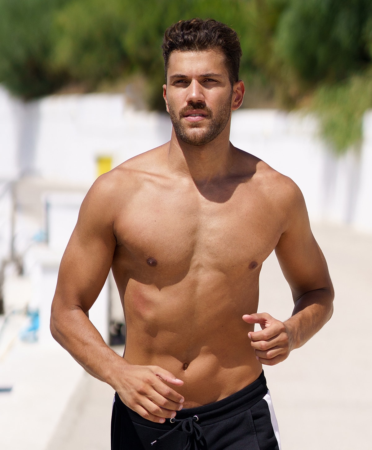 Shirtless man jogging outdoors in sunny setting.