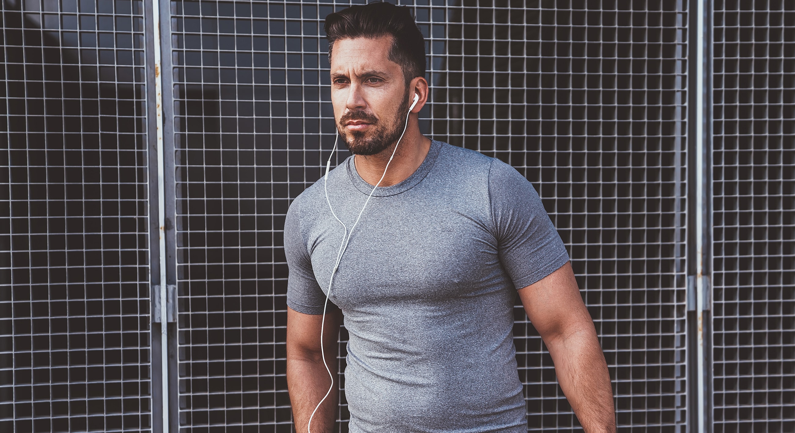 Man in gray shirt listening to music outdoors.